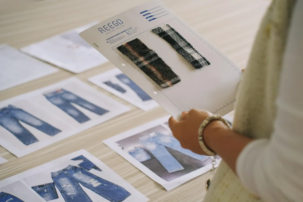 A designer reviewing a denim tech pack and matching fabric samples for custom jeans sample development.