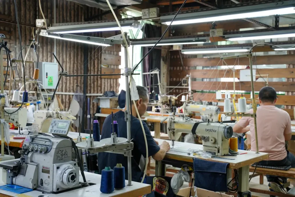 Workers sewing custom jeans on an OEM denim garment production line in a manufacturing factory.