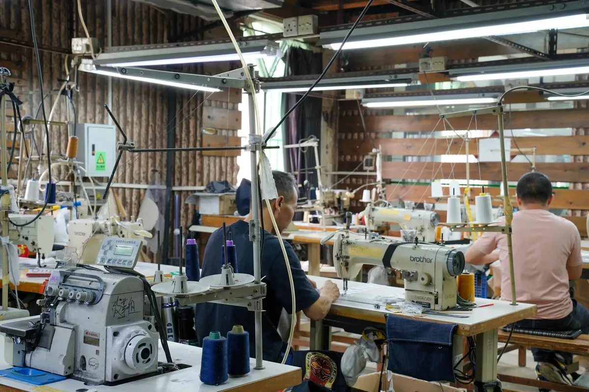 Factory workers operating sewing machines on a denim garment production line demonstrating manufacturing capability