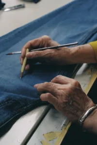 Skilled craftsman hand marking denim jeans with pencil showing artisan quality and attention to detail in luxury manufacturing