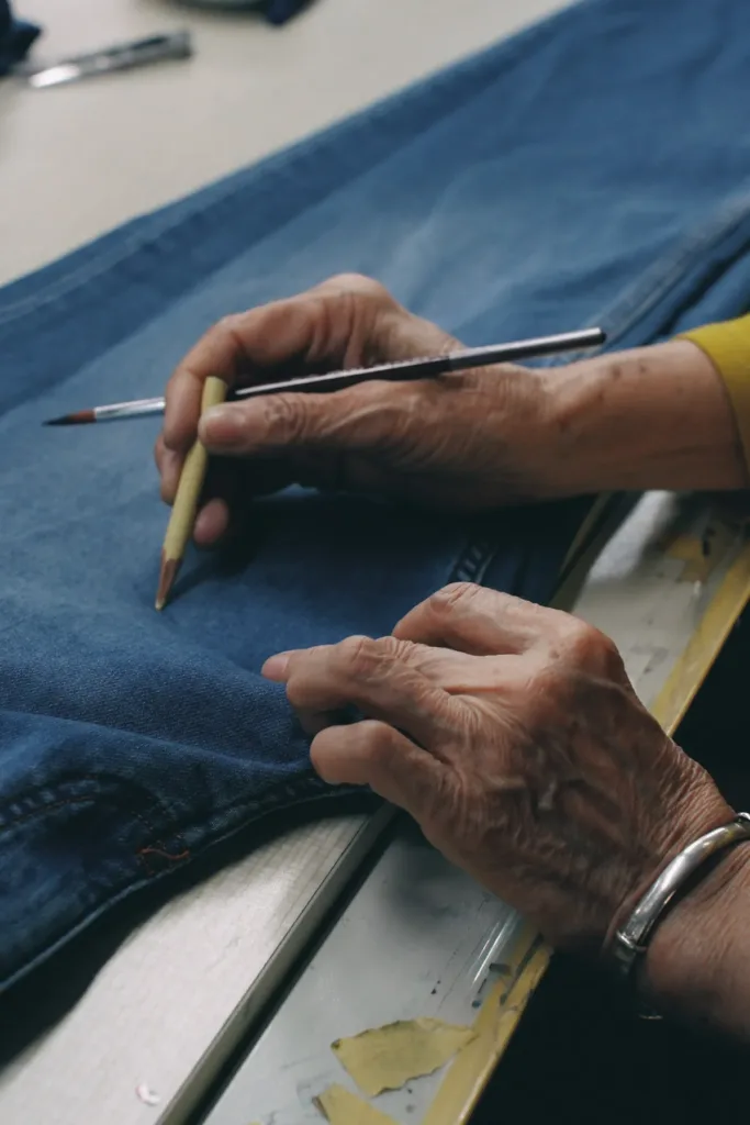 Skilled craftsman hand marking denim jeans with pencil showing artisan quality and attention to detail in luxury manufacturing