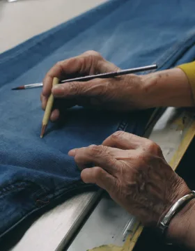 Skilled craftsman hand marking denim jeans with pencil showing artisan quality and attention to detail in luxury manufacturing