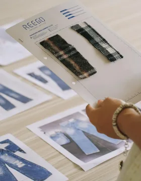 A designer reviewing a denim tech pack and matching fabric samples for custom jeans sample development.